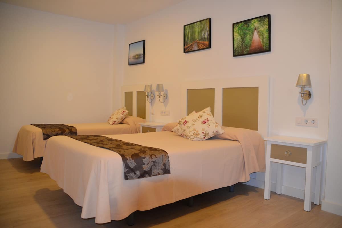 A hotel room with two beds, a nightstand, a lamp, and wall art.