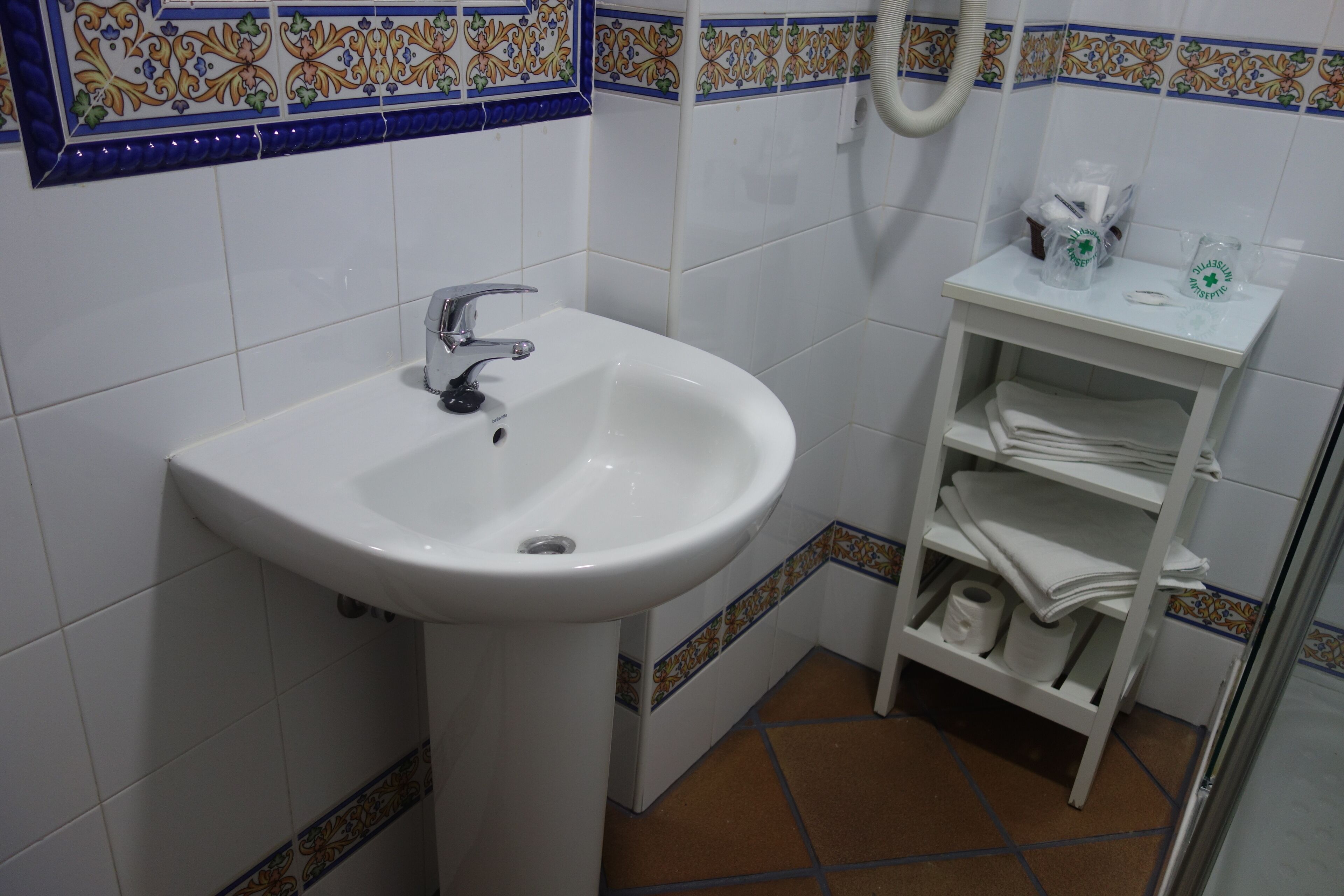 Une salle de bain avec un lavabo blanc, un porte-serviettes et une étagère contenant des articles de toilette.