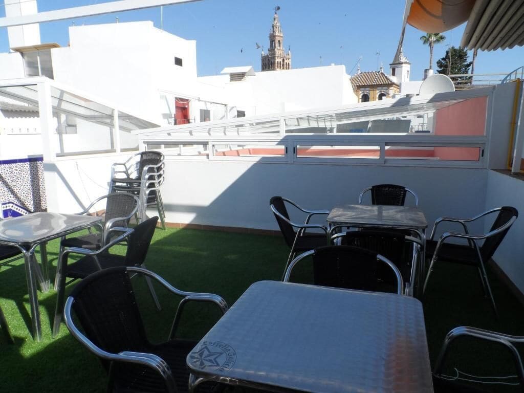 An outdoor patio with metal tables and chairs, a grill, and a view of a white building with a tower in the background.