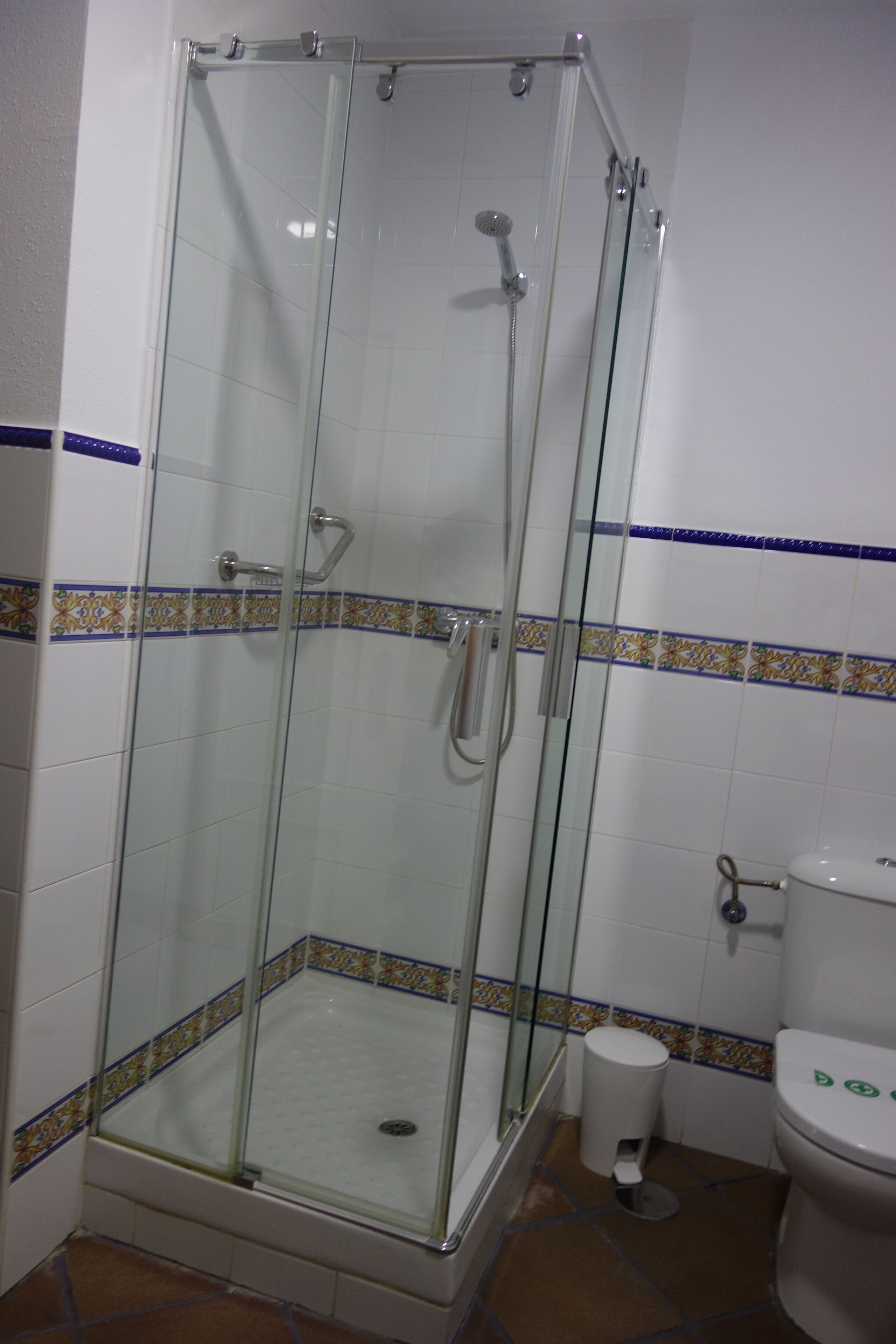 A glass-enclosed shower stall with a handheld showerhead and a handheld faucet.