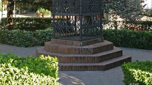 A wrought iron gazebo with intricate designs and lanterns, surrounded by well-maintained greenery and a building with yellow accents in the background. - Hotel Doña Lina (Seville)