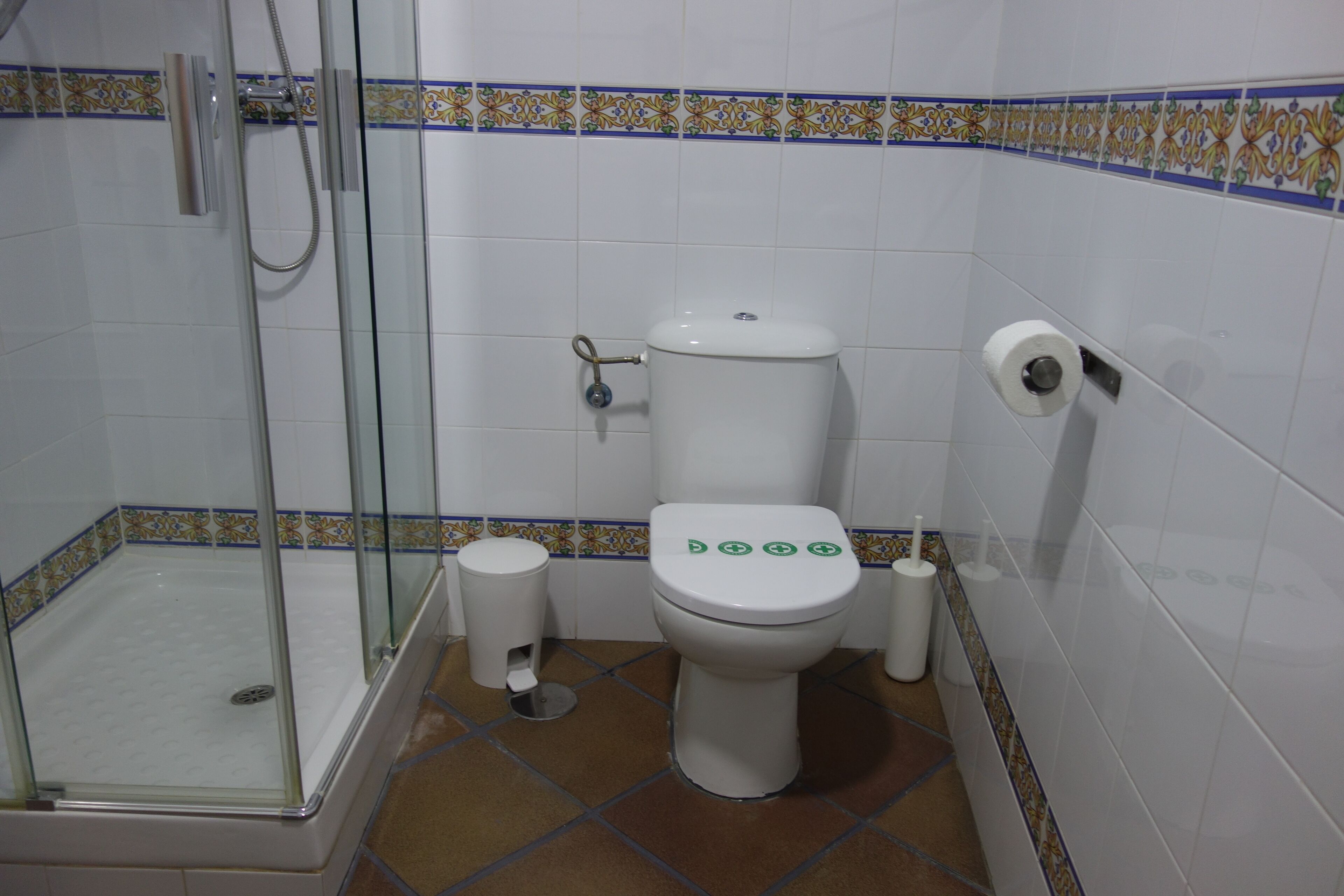 A bathroom with a glass-enclosed shower, a toilet with flush buttons, and a toilet paper holder.