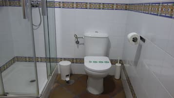 A bathroom with a glass-enclosed shower, a toilet with flush buttons, and a toilet paper holder.
