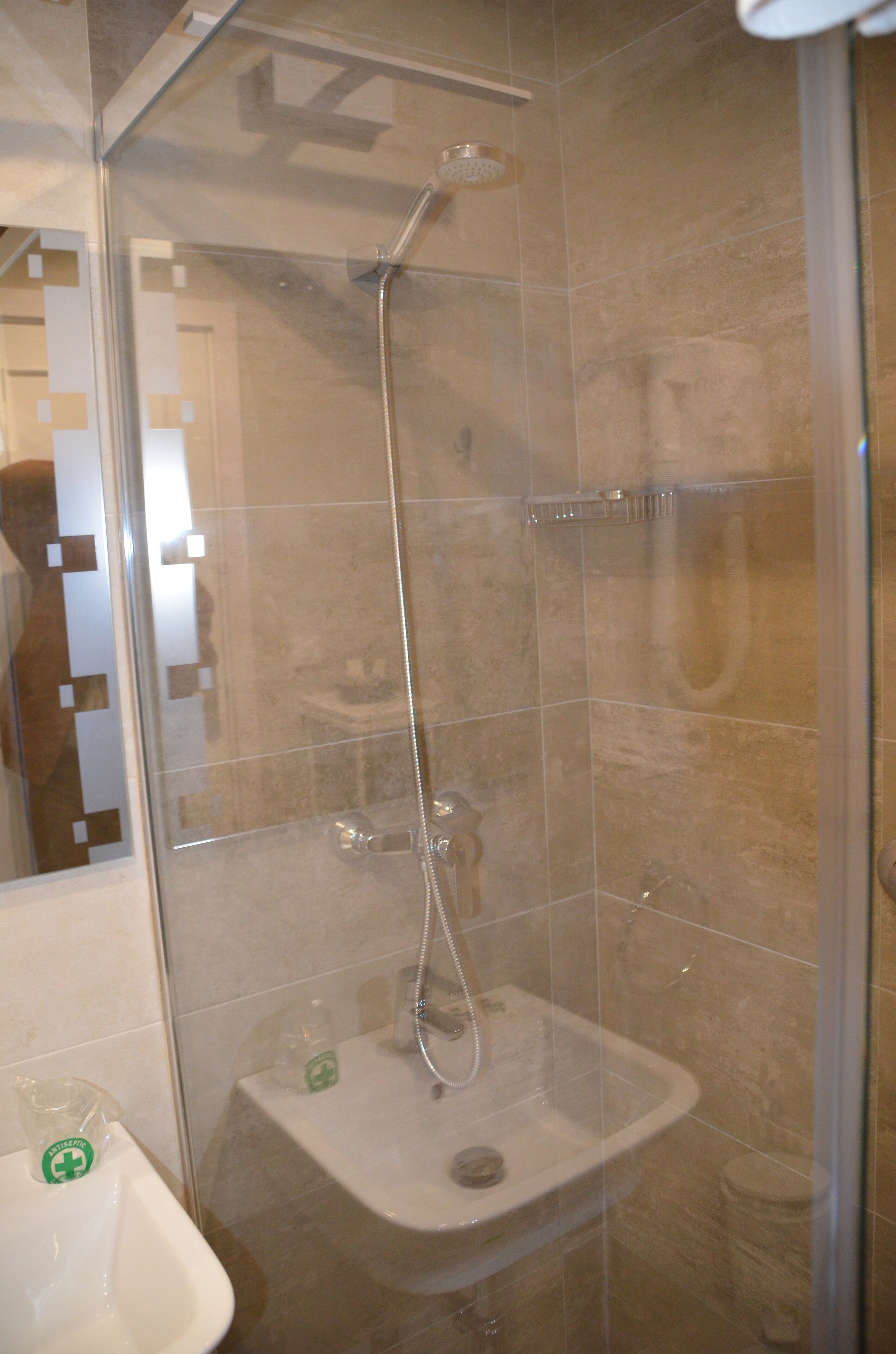 A glass-enclosed shower with a handheld showerhead and a wall-mounted faucet.