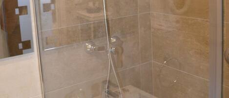 A glass-enclosed shower with a handheld showerhead and a wall-mounted faucet.