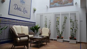 A cozy lounge area with wicker furniture, a decorative wall with a framed artwork, and a tiled floor. - Hotel Doña Lina (Seville)