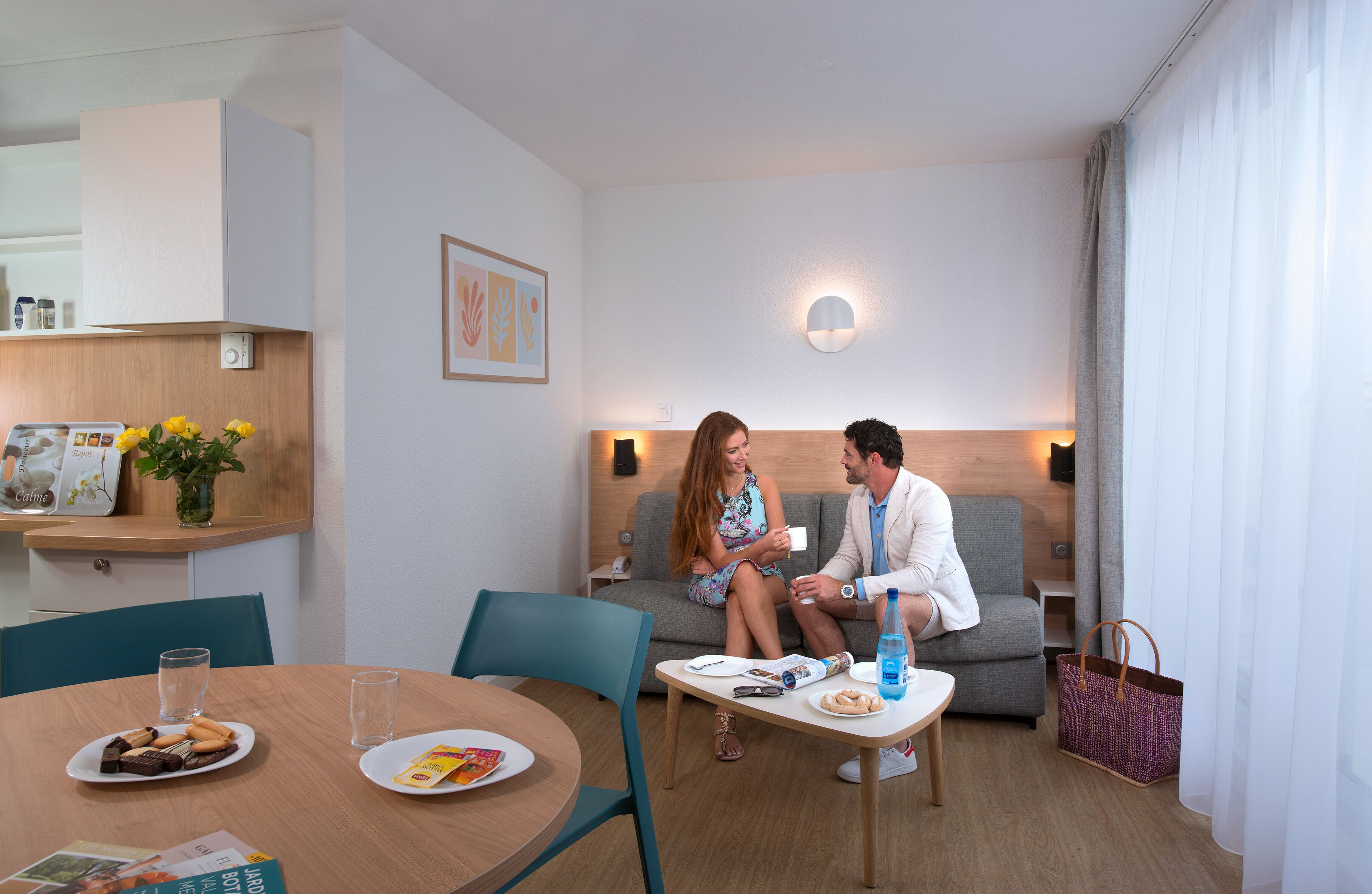 Ein modernes Hotelzimmer mit Essbereich, einer Couch und einem kleinen Tisch mit einer Flasche und einem Korb.