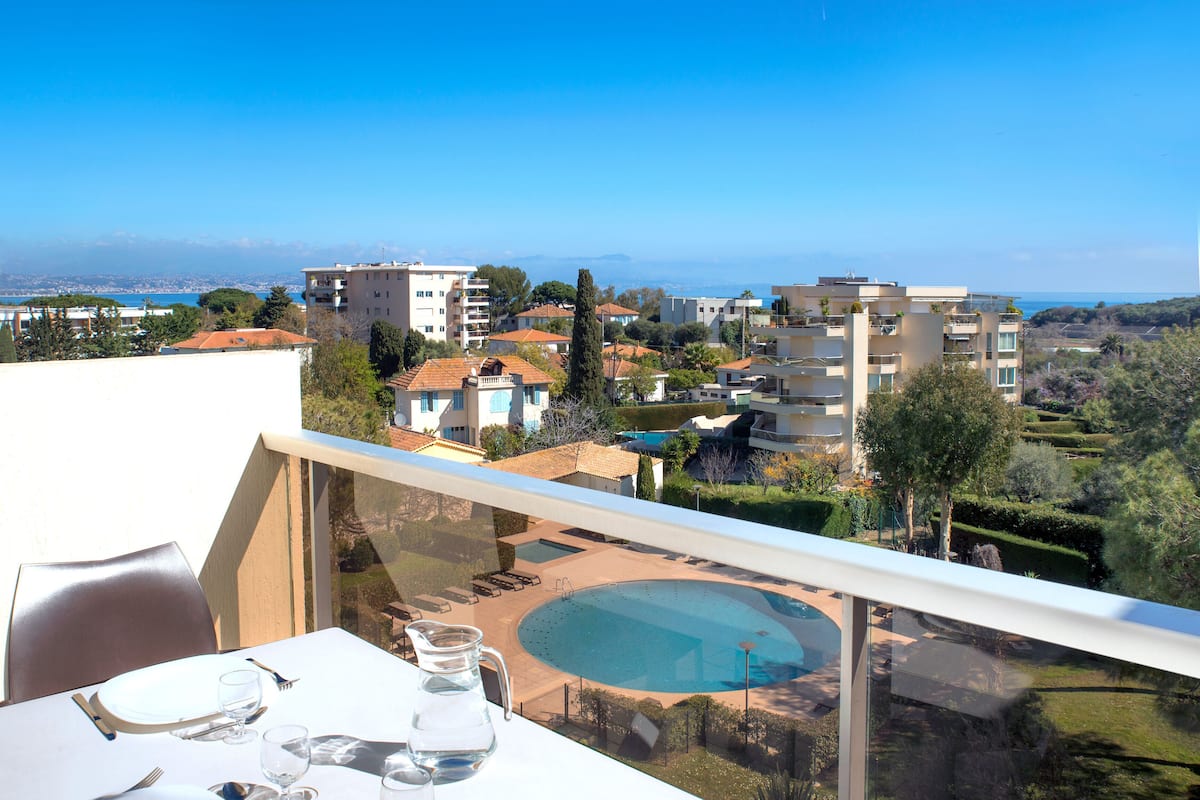 Varanda com mesa posta para refeições, vista para uma piscina e área residencial.