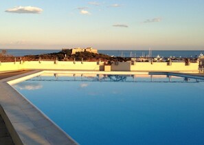 A swimming pool with a view of a coastal area, including a castle-like structure and boats.