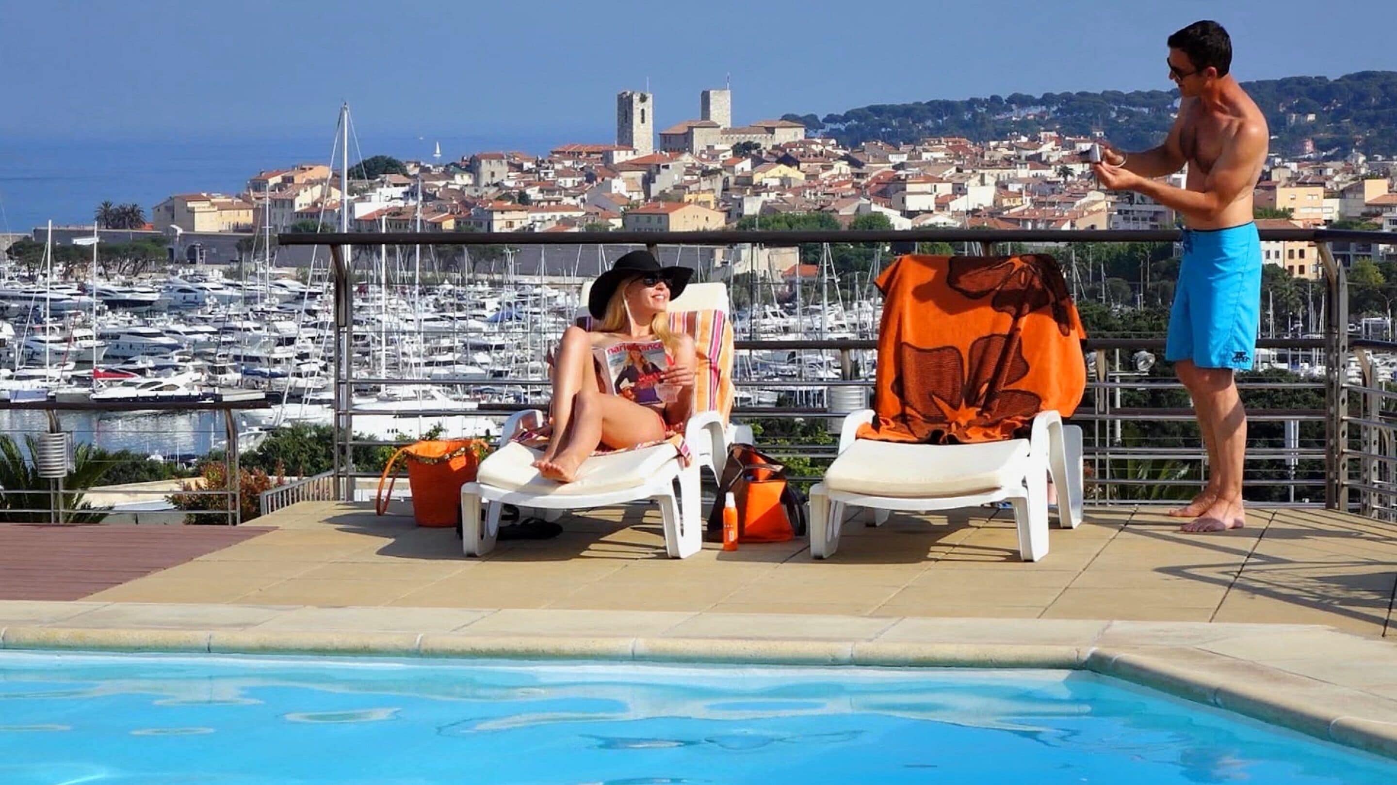 Ein Poolbereich mit Liegestühlen, Blick auf eine Marina und eine Stadt im Hintergrund.