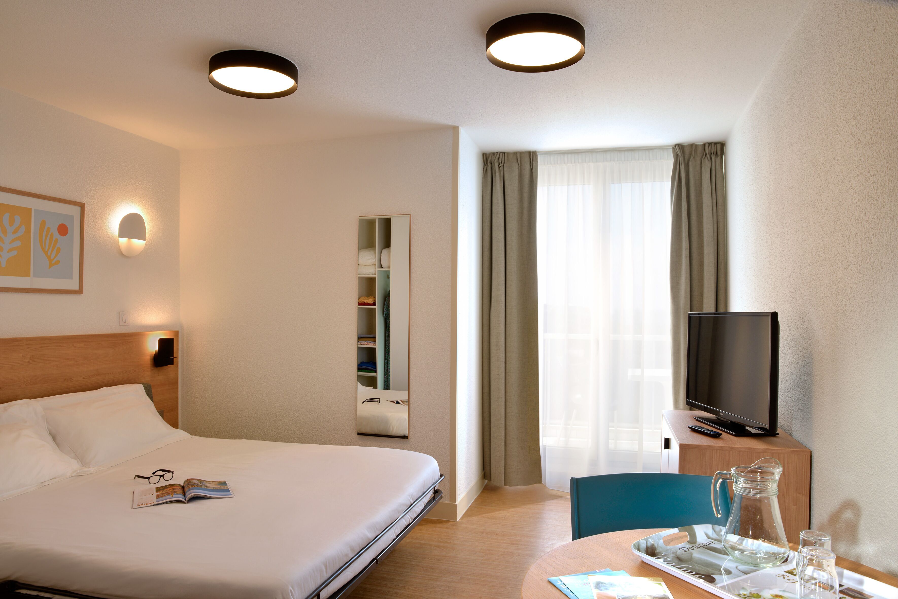 Une chambre d’hôtel avec un lit, une table de chevet, une télévision et une fenêtre avec des rideaux.
