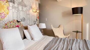 A bedroom with a bed, a lamp, a chair, and a wall with a floral and architectural design.