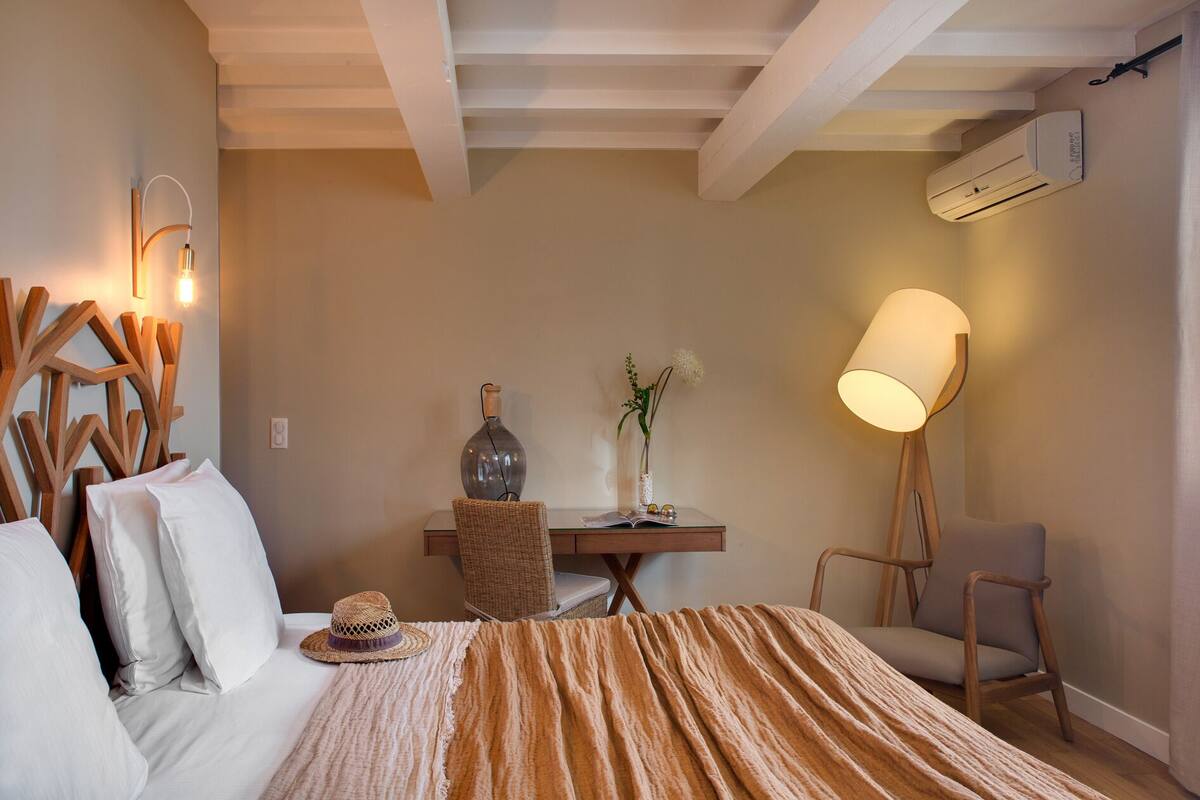 A bedroom with a bed, a desk, a chair, a floor lamp, and a wall-mounted air conditioner.