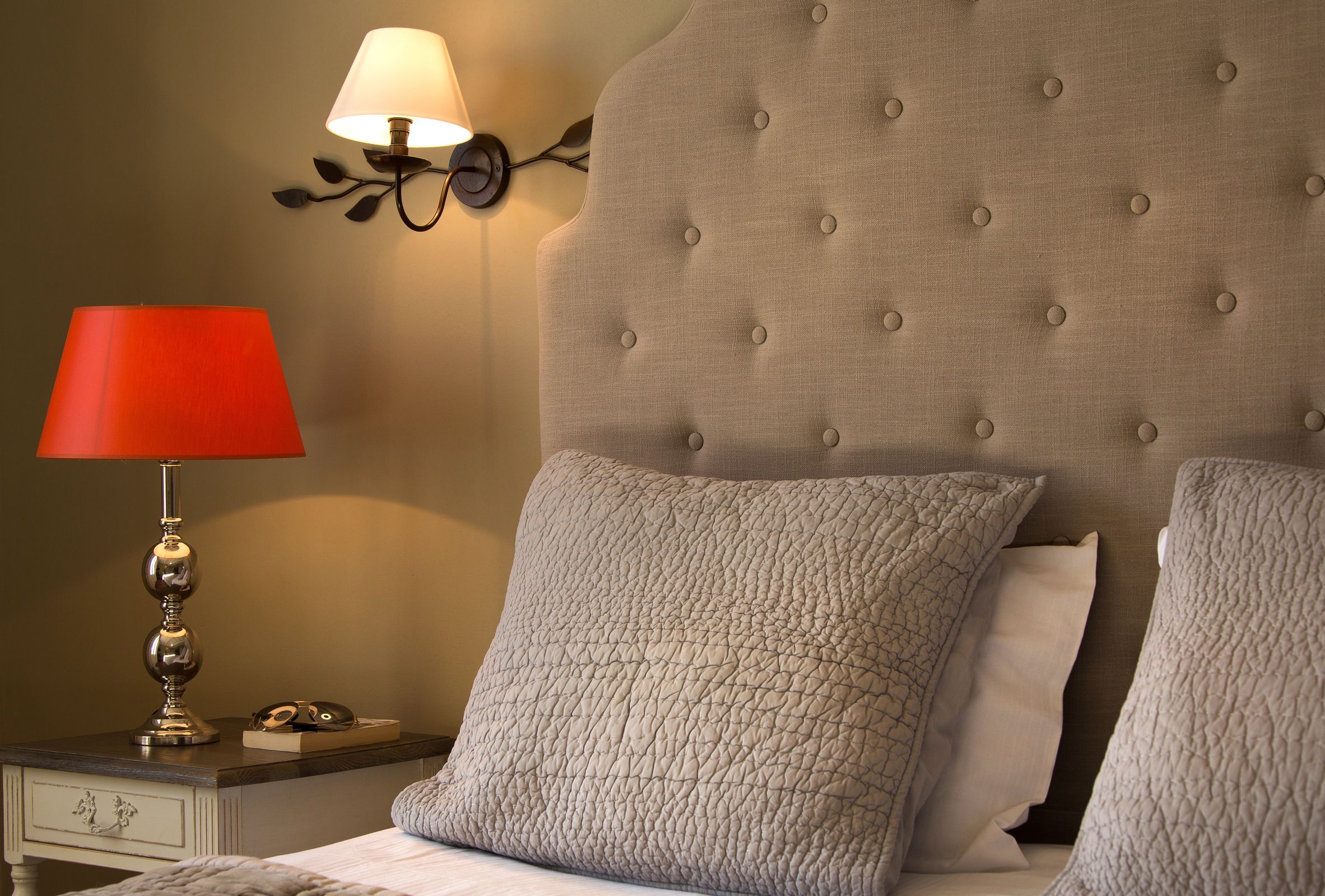Cama bem arrumada com duas almofadas, abajur e luminária na parede.