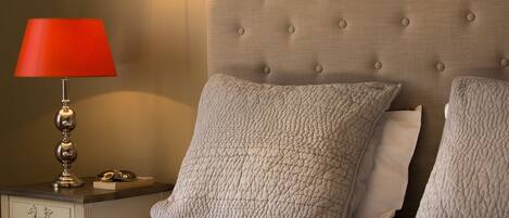 Una cama bien hecha con dos almohadas, una lámpara de noche y una lámpara de pared.