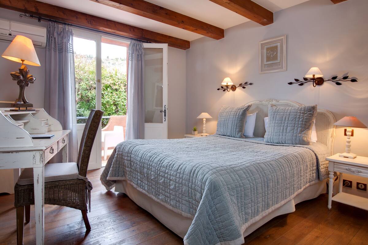A bedroom with a bed, a desk, a chair, and a nightstand.