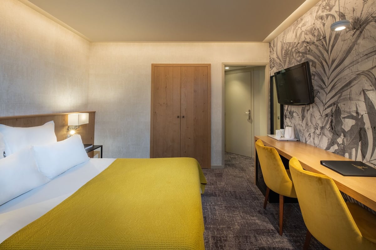 Une chambre d’hôtel comprenant un lit, un bureau, deux chaises, une télévision et une porte donnant sur une autre pièce.