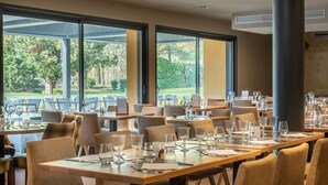 Een restaurant met gedekte tafels, grote ramen met uitzicht op de omgeving, en een modern interieur.