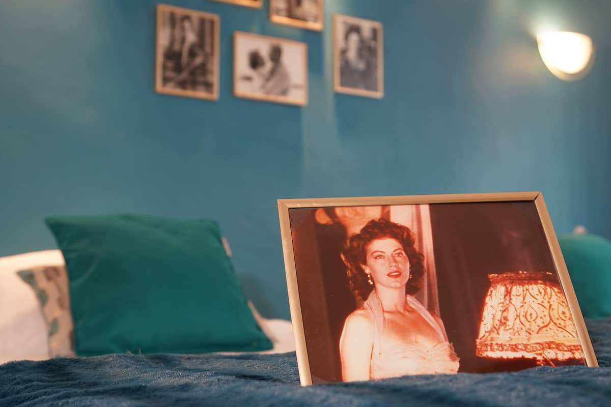 A framed photograph on a bed with teal pillows and a patterned lamp.