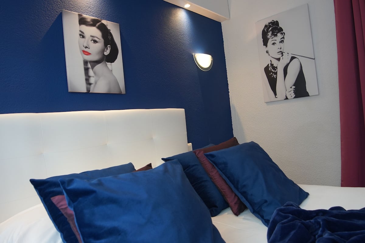 A hotel room with a large bed, blue pillows, and two wall-mounted pictures.