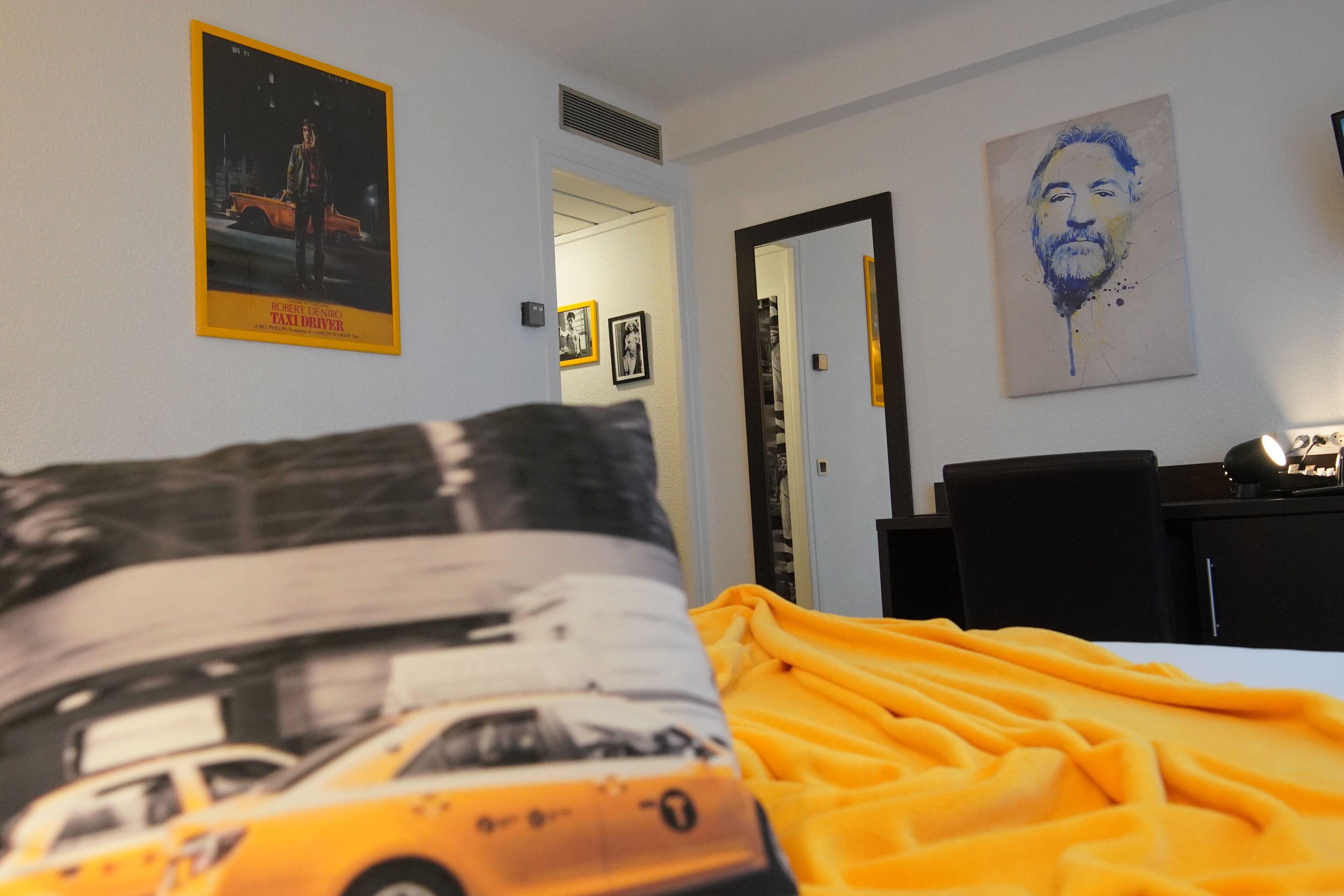 A hotel room with a bed, a poster on the wall, and a painting.