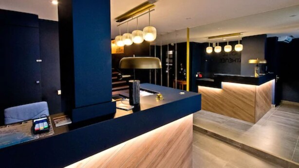 A modern reception desk with a dark blue counter, a black lamp, and a wooden reception area. - ATH Hôtel Athénée (Cannes)