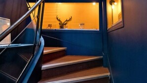 A staircase with a wooden handrail and carpeted steps leading to a landing with a glass enclosure. - ATH Hôtel Athénée (Cannes)