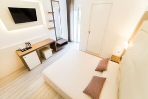 A modern hotel room with a flat-screen TV, a wooden desk with a coffee maker, a small cabinet, a bed with two pillows, and a large mirror. - Hotel All'Orologio (Caorle)
