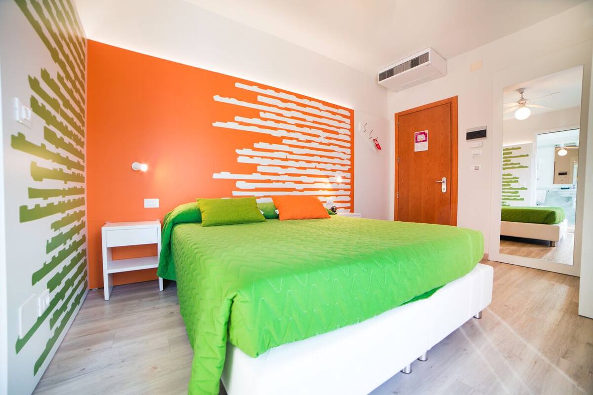 A modern bedroom with a large bed, an orange accent wall, and a wooden floor.