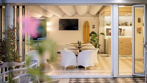 Un patio interior moderno con mobiliario de mimbre blanco, una tabla de surf y un televisor de pantalla plana en la pared.
