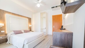 Una habitación de hotel moderna con una cama grande, mesitas de noche, un cabecero de madera, televisión y una pequeña zona con kitchenette.