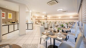 Un comedor amplio con varias mesas y sillas, una barra de buffet y una cocina al fondo.