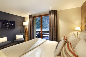 Quarto de hotel com cama, duas cadeiras, mesa de cabeceira de madeira, luminária e vista para o exterior.