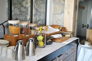 Um buffet de café da manhã com diversos alimentos, jarras de café e um fundo de parede de pedra.