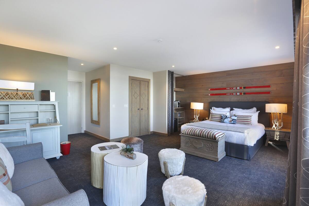 A modern hotel room with a large bed, a desk, a sofa, and a small round table.