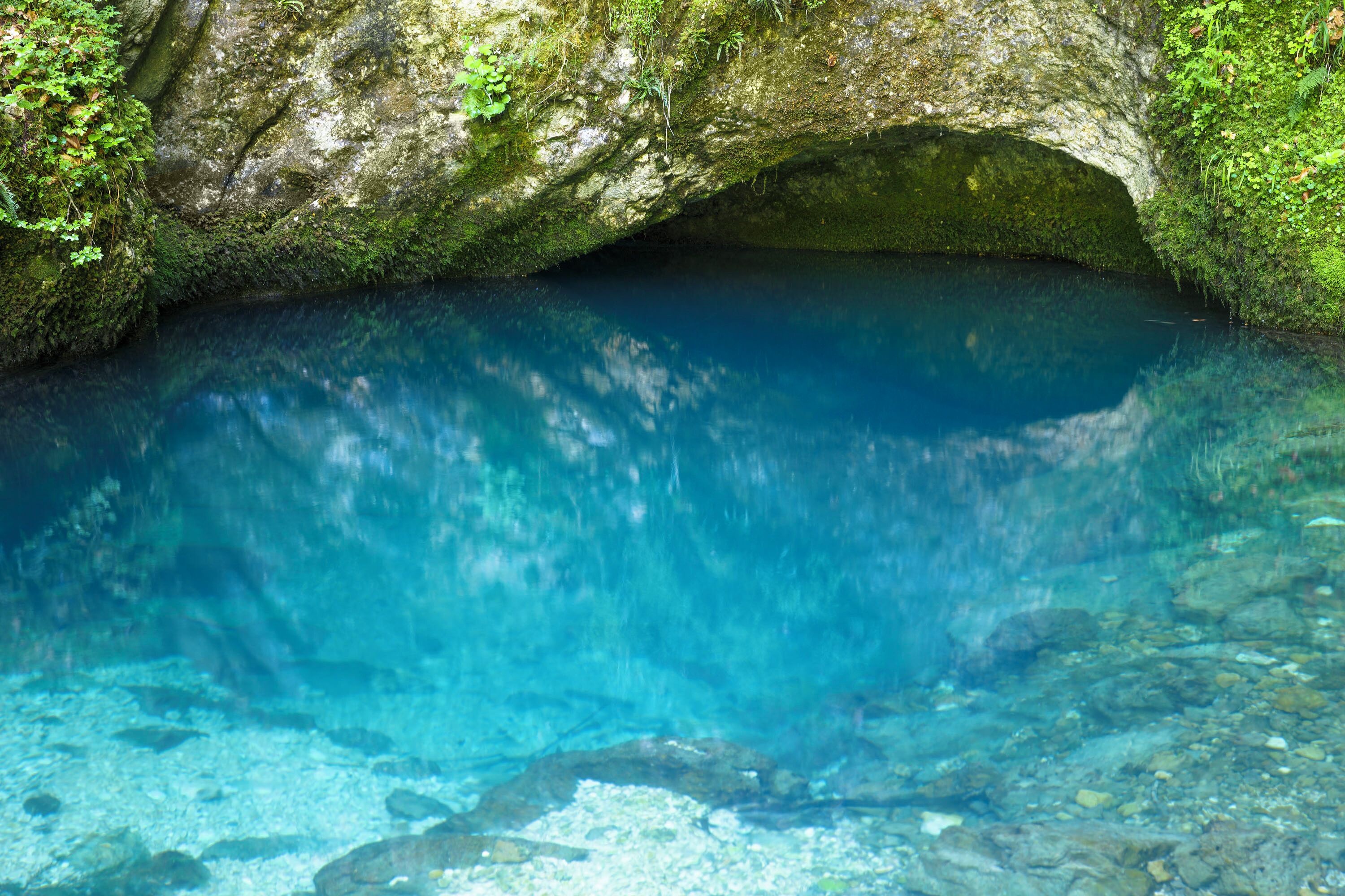 Une grotte naturelle avec de l’eau claire, des rochers couverts de mousse et un sol rocheux.