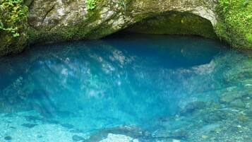 A natural cave with clear water, moss-covered rocks, and a rocky floor.