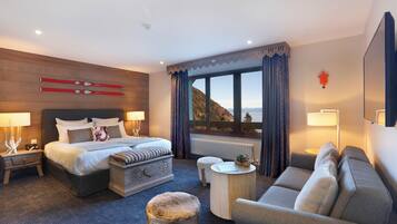 A hotel room with a large bed, a sofa, a small table, and a view of the mountains.