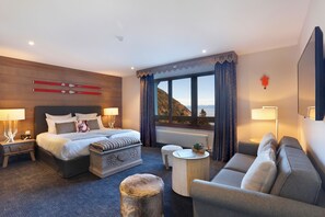 A hotel room with a large bed, a sofa, a small table, and a view of the mountains. - Chalet Hôtel La Mainaz Restaurant & Resort (Mijoux)