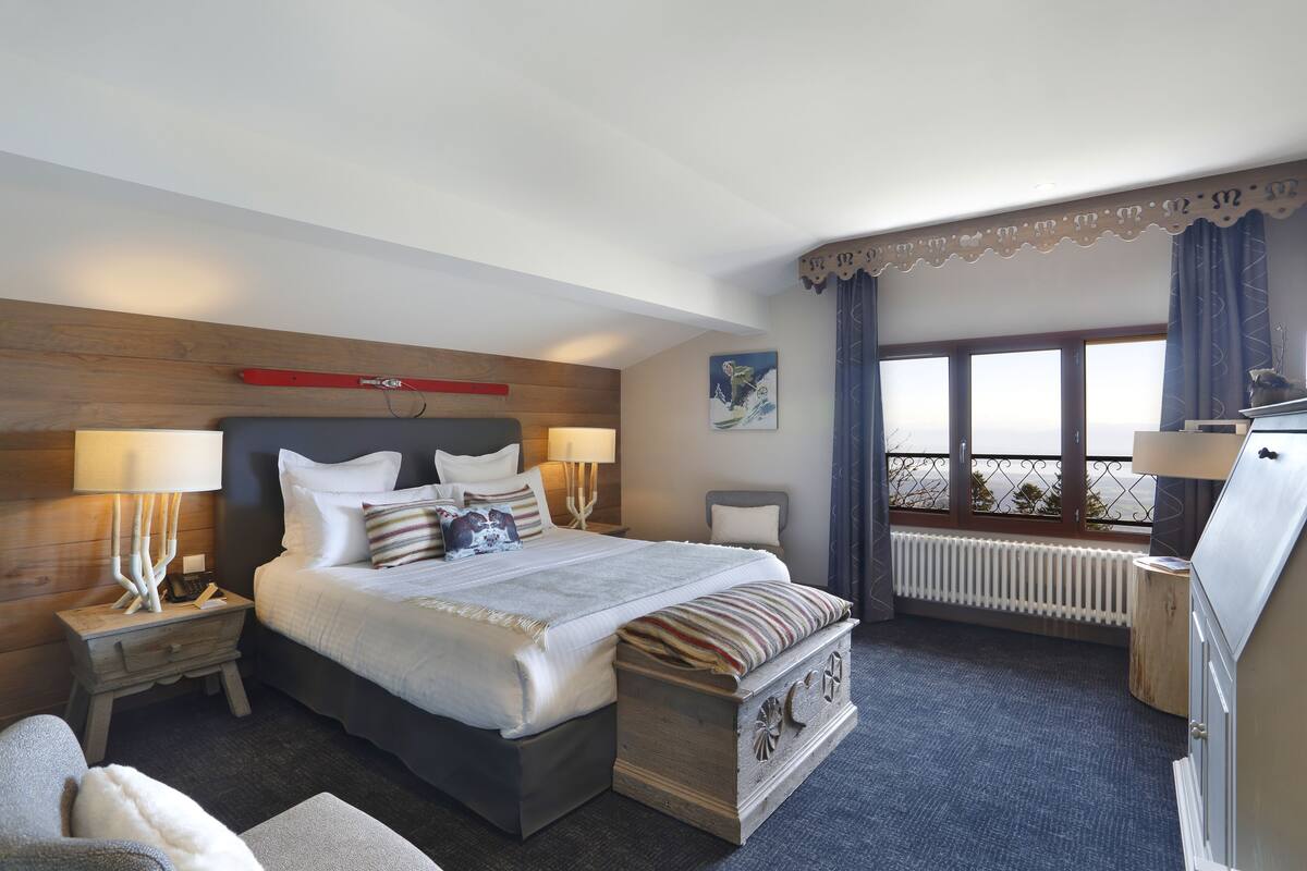 A hotel room with a large bed, bedside tables, a dresser, a radiator, and a window with a view.