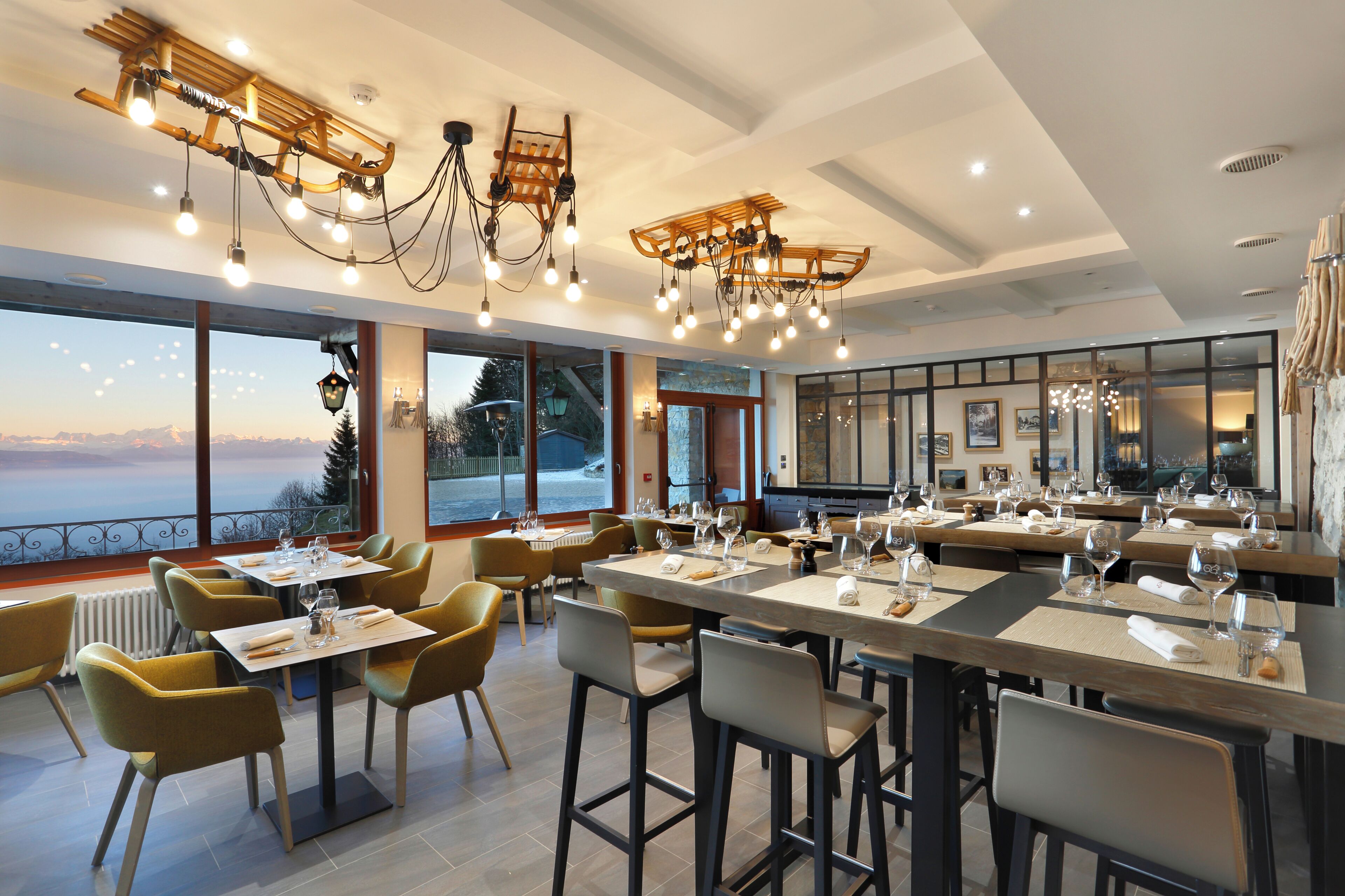 Un ristorante con diversi tavoli e sedie, ampie finestre che offrono vista sull'esterno e un lampadario moderno.