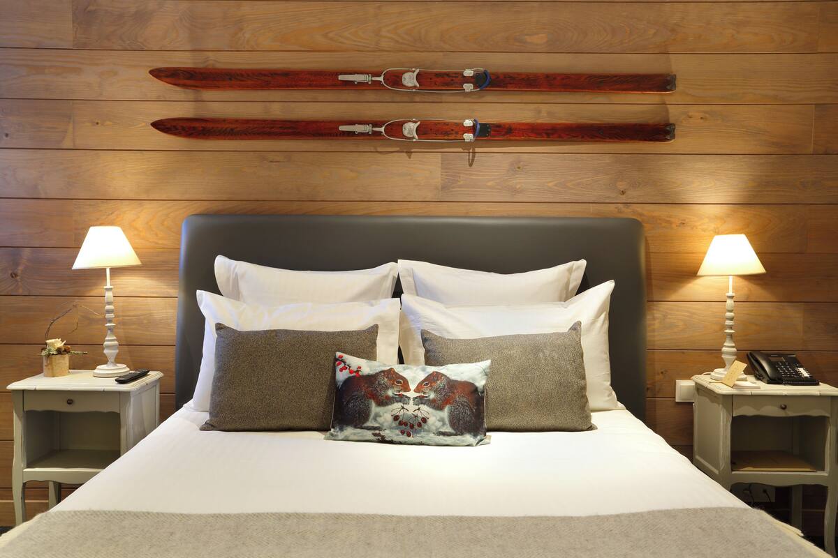 A bed with white and brown bedding, two bedside tables with lamps, and skis mounted on the wall.