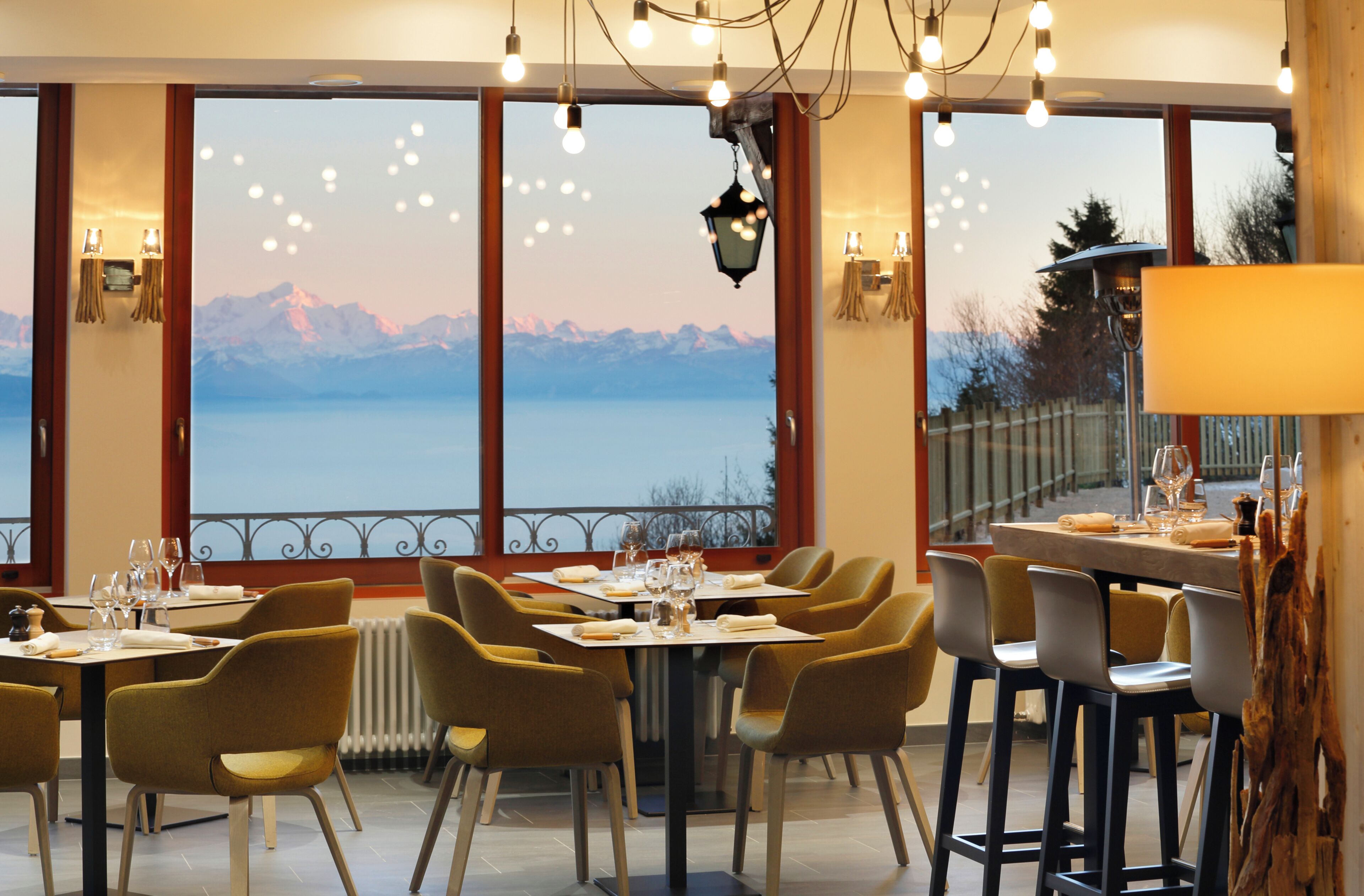 A restaurant with tables set for dining, chairs, and a view of mountains through large windows.