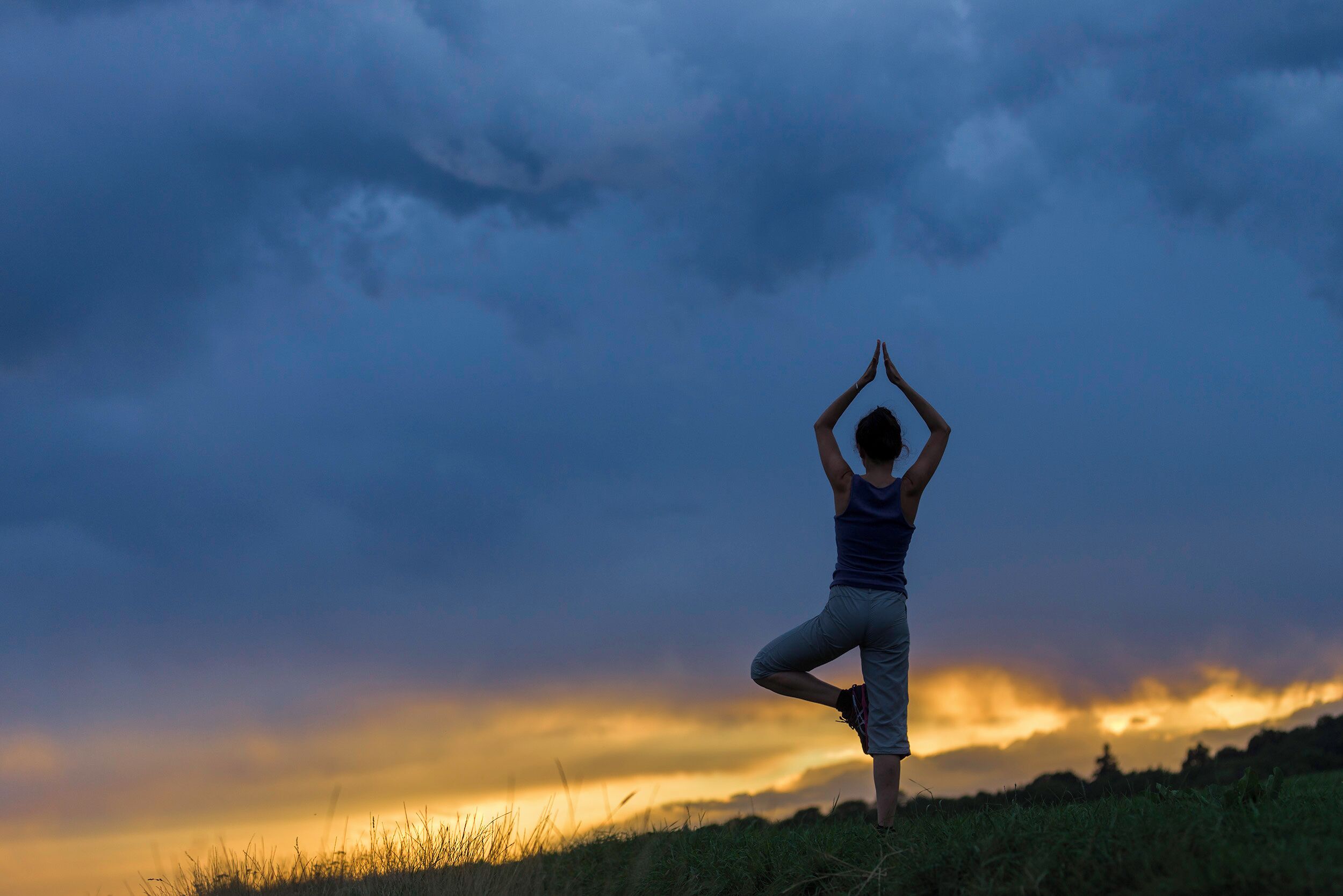A person performing a yoga pose on a grassy field with a sunset in the background.