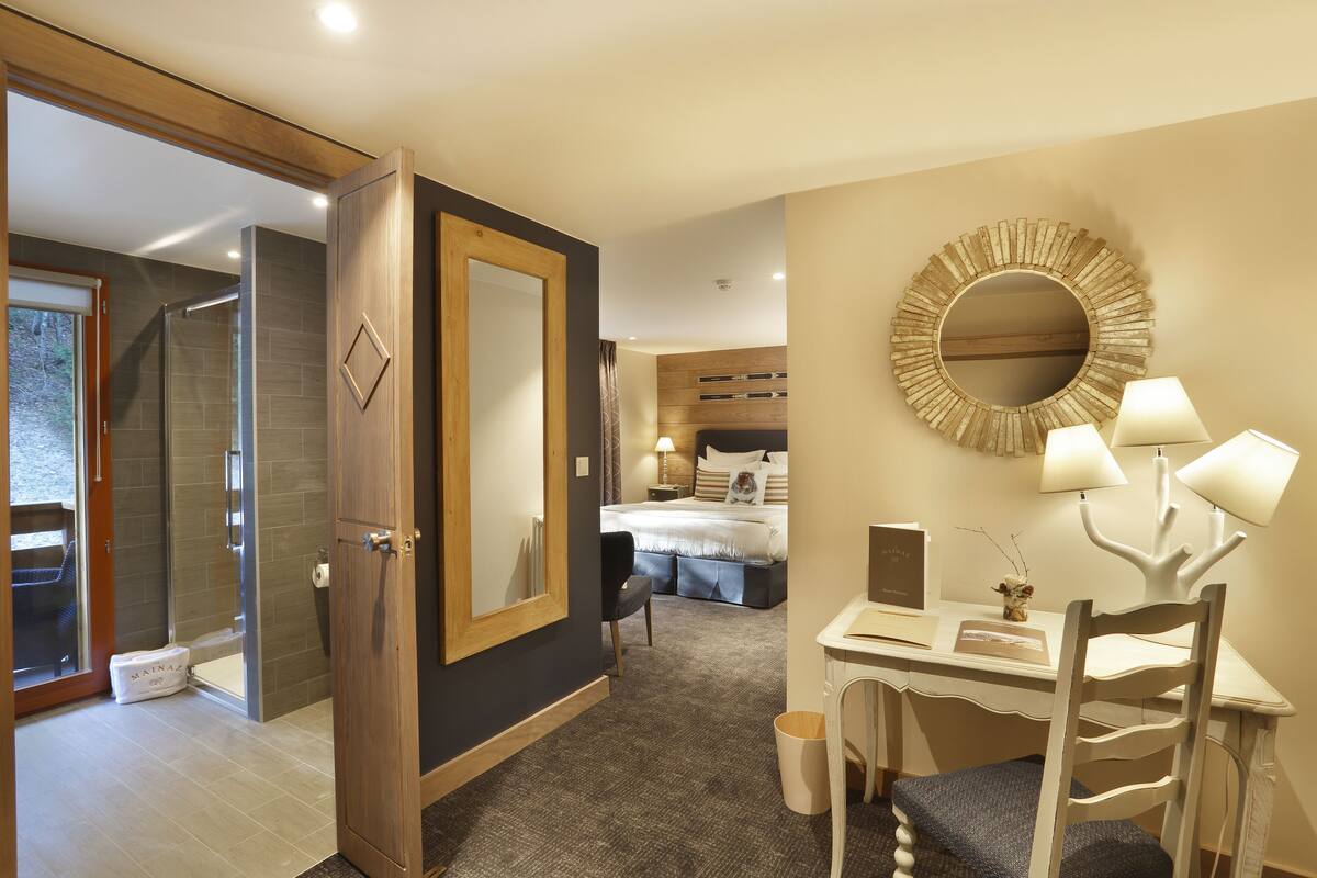 A hotel room with a shower, a bed, a desk with a lamp, and a mirror.