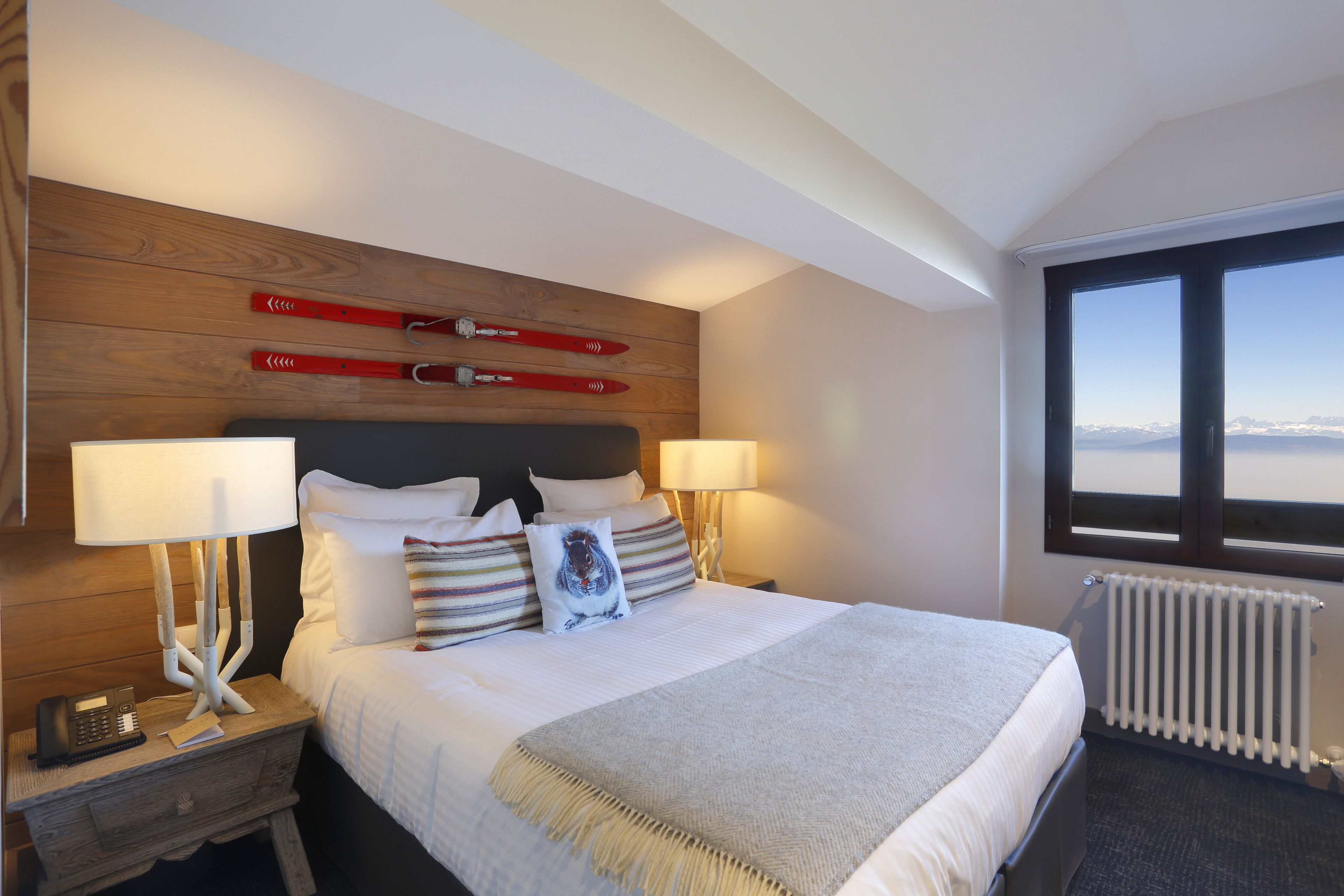 Camera d'albergo con un letto grande, una testiera in legno, due lampade da comodino, un comodino, una finestra con vista e un termosifone.