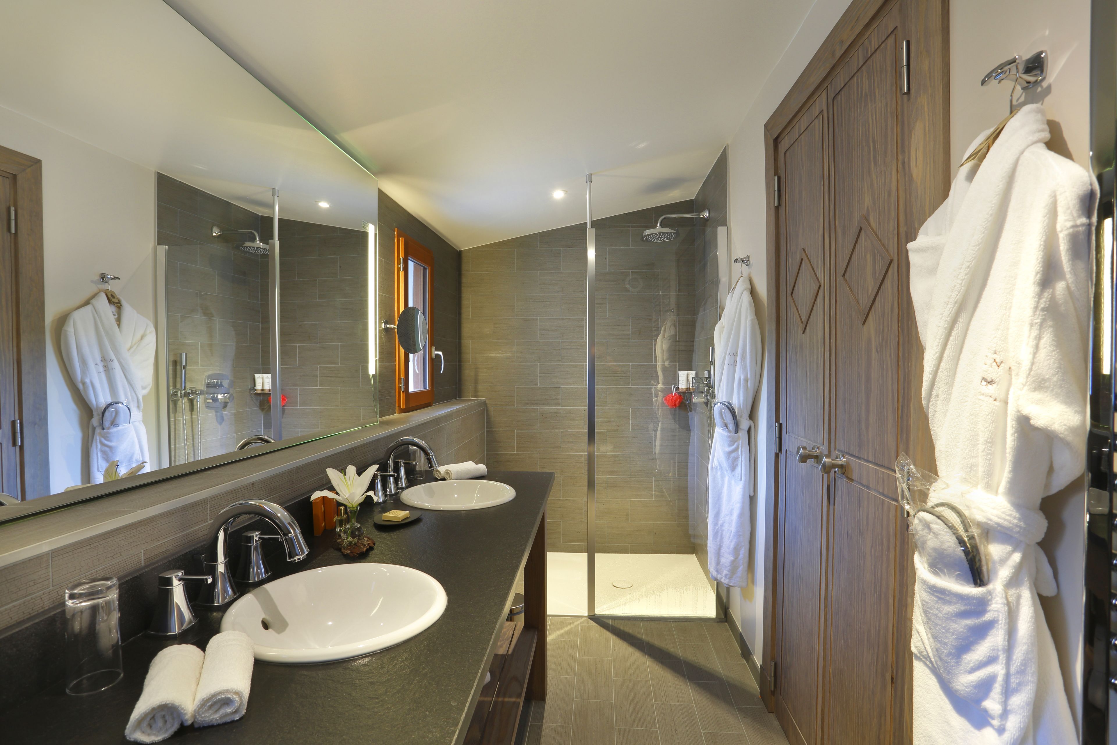 Een moderne badkamer met twee wastafels, een glazen douchecabine en een houten garderobe.