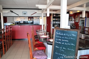 En restaurant med barområde, et tavleskilt med menu og et køkken i baggrunden.