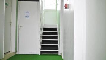 A narrow hallway with a white door at the end, a green carpet, and a staircase leading to a landing.