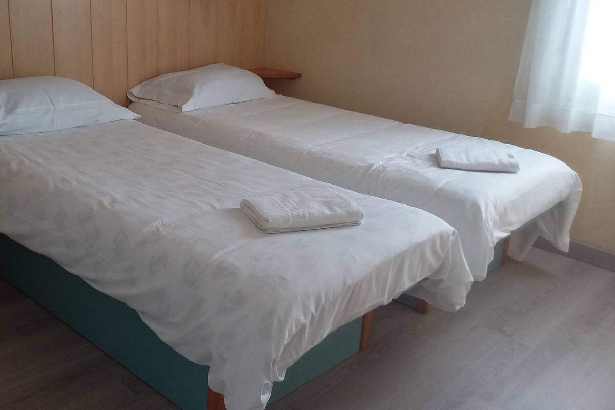 Two single beds with white linens and pillows, a wooden headboard, and a wooden floor.